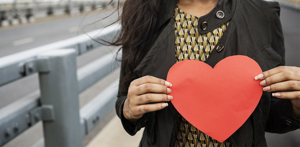 A woman holding a paper heart in front of her chest.