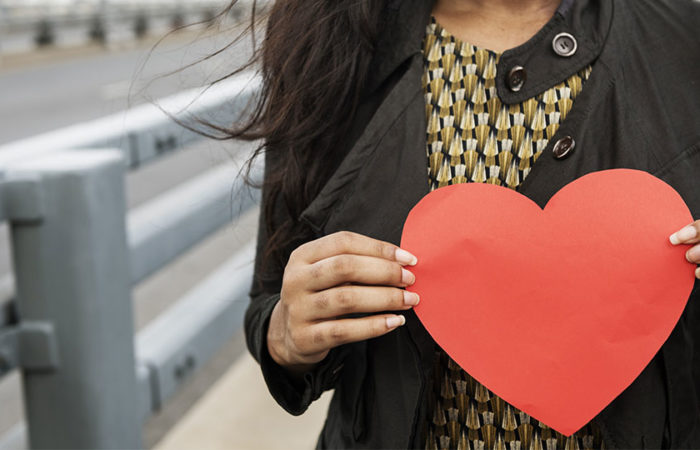 A woman holding a paper heart in front of her chest.